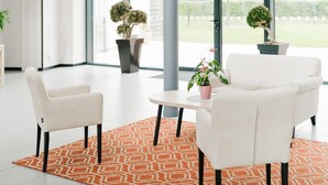 Un espacio interior moderno con dos sillas blancas, una mesita redonda y una alfombra estampada.