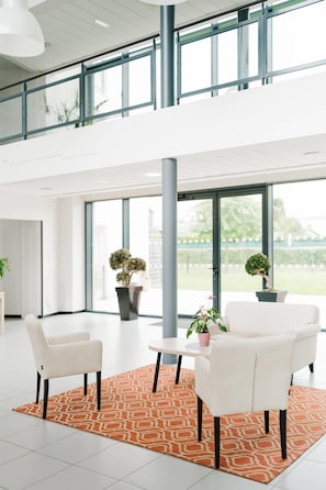 Een moderne binnenruimte met twee witte stoelen, een klein rond tafeltje en een vloerkleed met een patroon.
