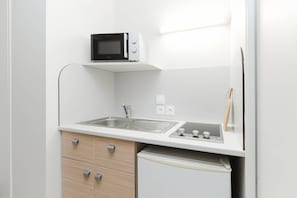 Een compact keukenhoekje met een magnetron, spoelbak en kleine koelkast.