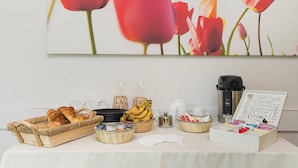 Une table dressée pour le petit-déjeuner avec du pain, des bananes et du café, accompagnée d’une machine à café et d’un panier de croissants.