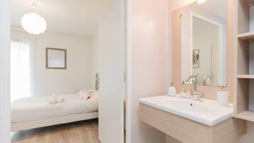 Une chambre moderne avec un lit, une table de chevet et un grand miroir au-dessus du lavabo.