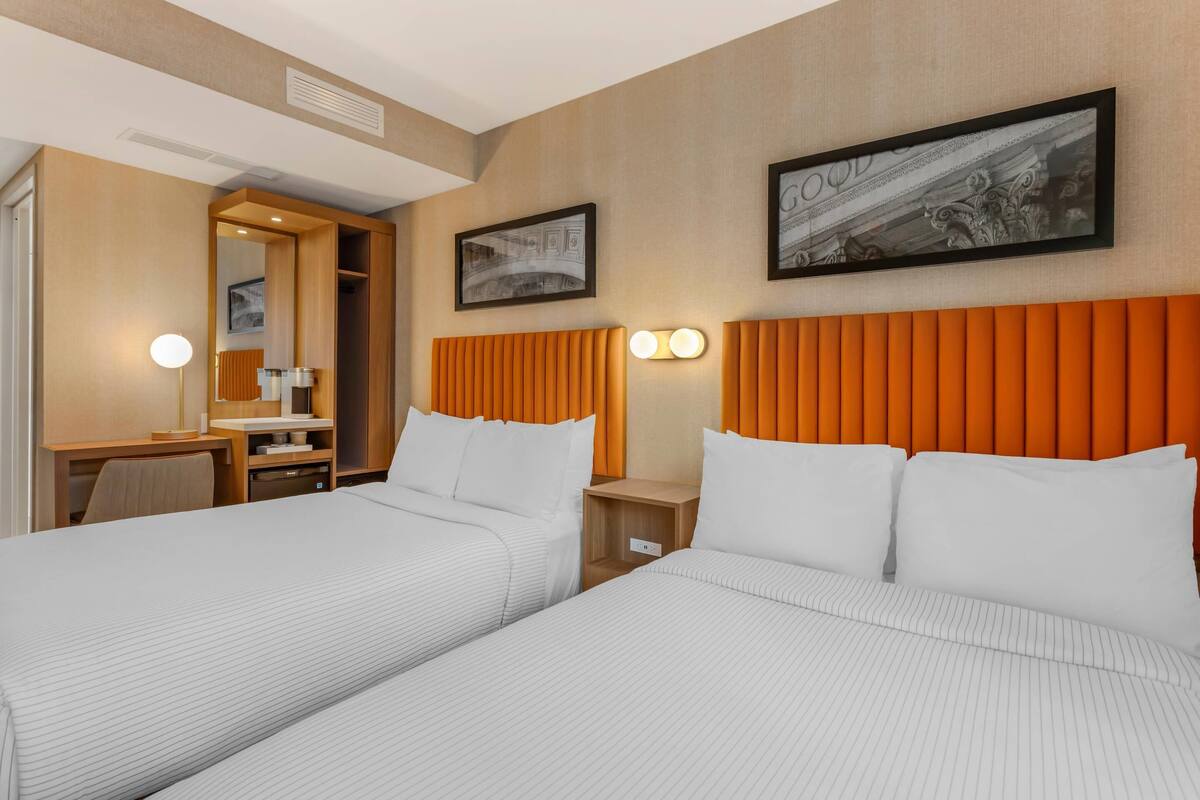 Habitación de hotel con dos camas, un escritorio, una silla y un armario.