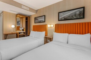 Quarto de hotel com duas camas, uma escrivaninha, uma cadeira e um guarda-roupa.
