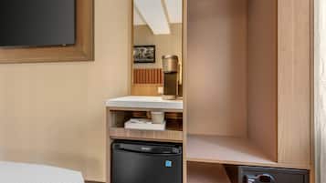 Une chambre d’hôtel compacte comprenant un lit, un mini-bar, un petit réfrigérateur, un coffre-fort intégré et un luminaire au plafond.