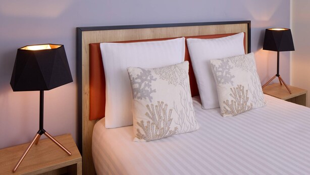 A neatly made bed with white bedding and two decorative pillows, flanked by two black lamps on wooden nightstands. - Quality Aparthotel Les rives de Mèze (Meze)