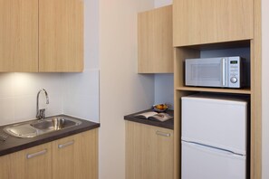 A kitchen with wooden cabinets, a stainless steel sink, a microwave, and a white refrigerator. - Quality Aparthotel Les rives de Mèze (Meze)