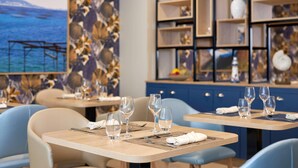 A restaurant with tables set for dining, featuring a coastal mural on the wall and a modern shelving unit with decorative items. - Quality Aparthotel Les rives de Mèze (Meze)
