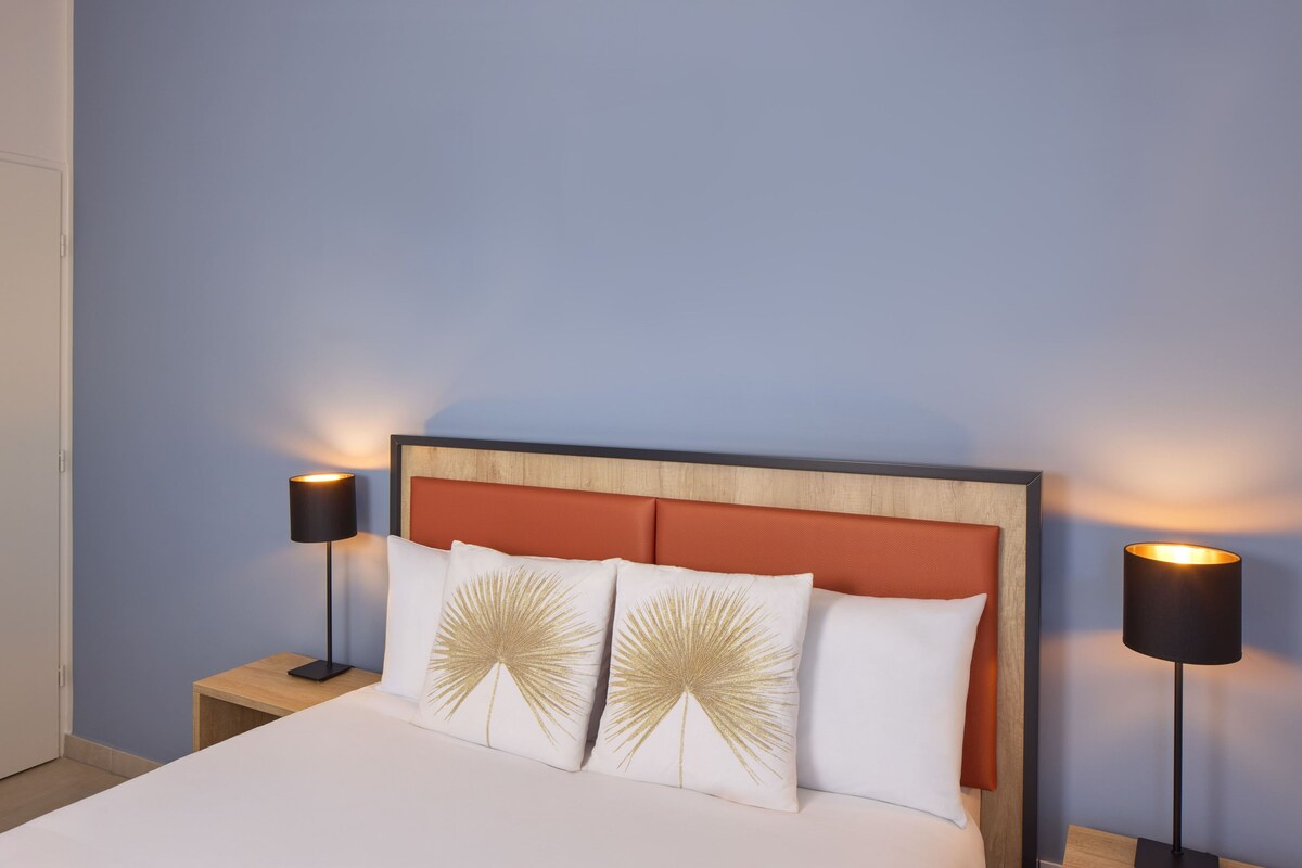 A neatly made bed with two decorative pillows, a wooden headboard, and two bedside lamps.