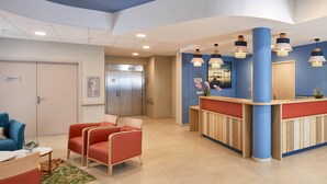 A reception area with a blue and white color scheme, a reception desk, a waiting area with red chairs, and an elevator. - Quality Aparthotel Les rives de Mèze (Meze)