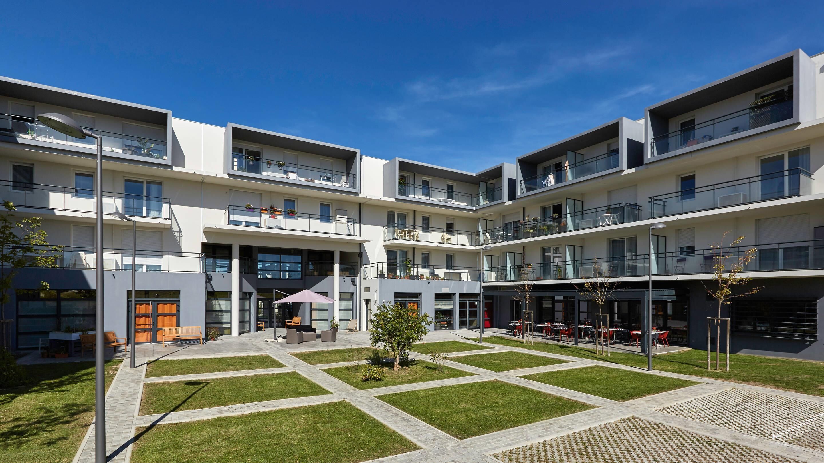 Un edificio moderno de varios pisos con áreas de estar al aire libre y un patio central.