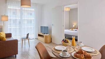 A modern hotel room with a dining area, a sofa, a TV, and a bed.