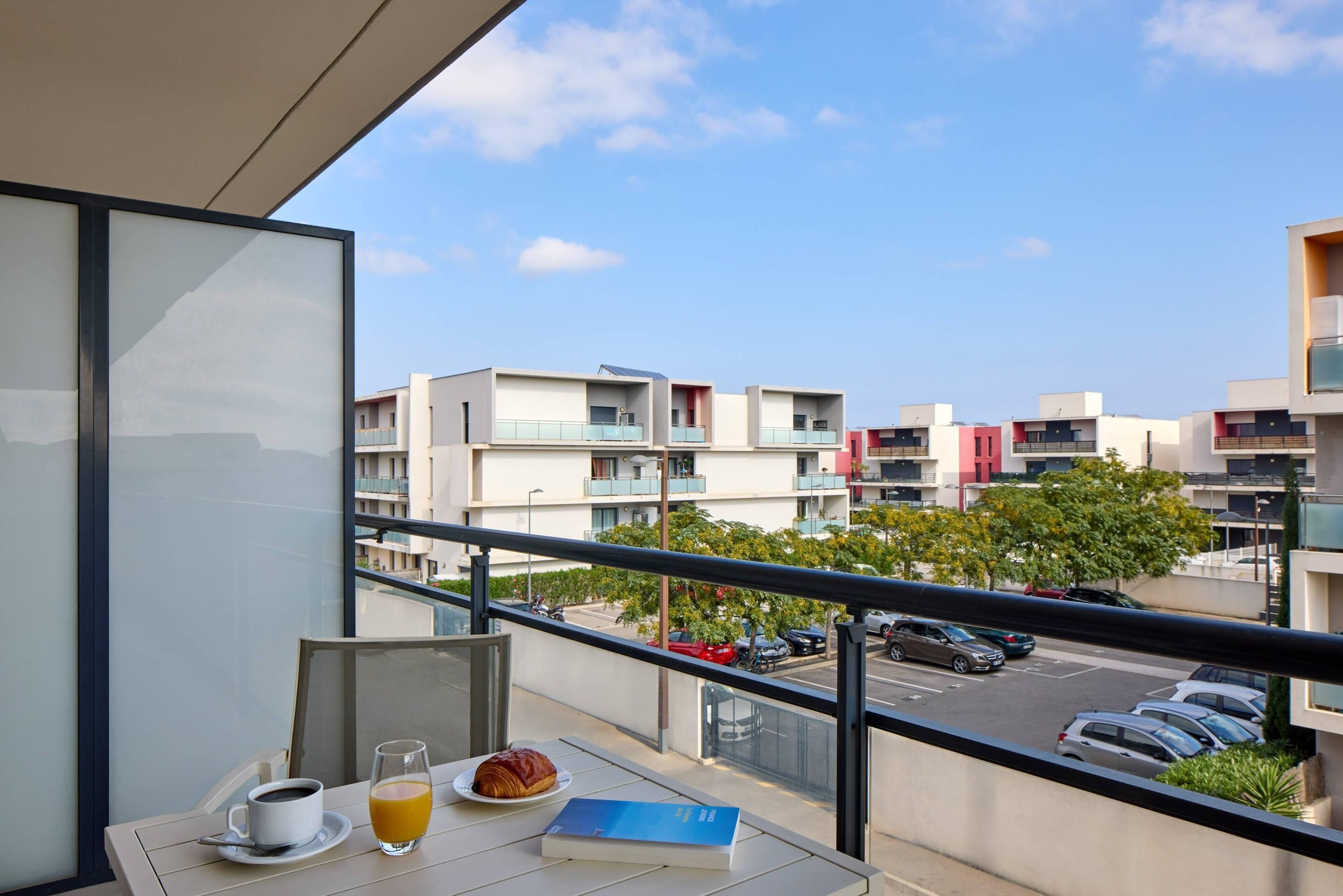 A balcony with a table set for breakfast, a book, and a glass of orange juice.