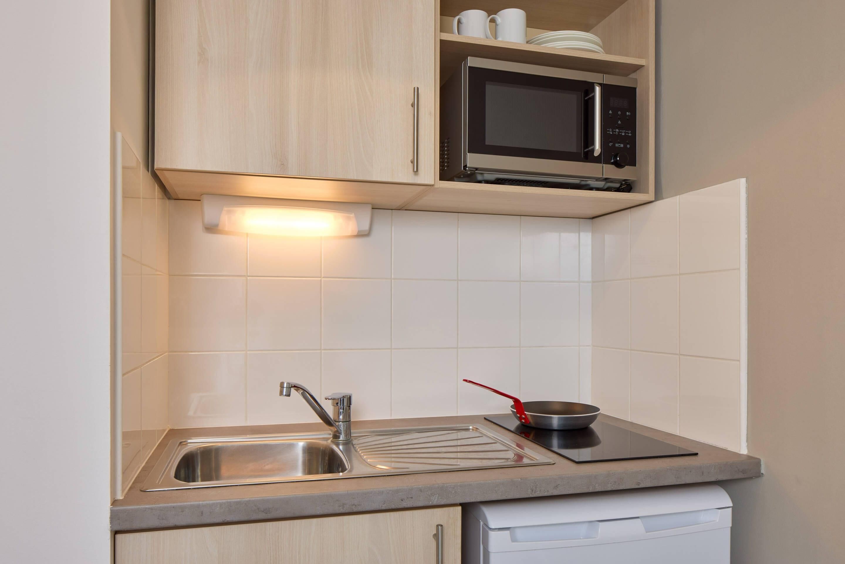 A kitchen with a stainless steel sink, a microwave, and a dish rack.