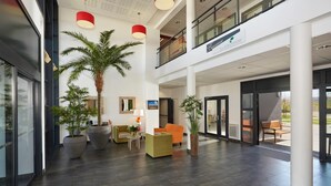 A spacious lobby with a high ceiling, modern furniture, and large potted plants.