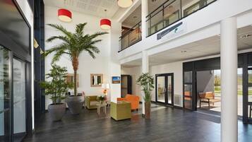 A spacious lobby with a high ceiling, modern furniture, and large potted plants.
