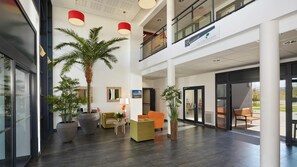 A spacious lobby with a high ceiling, modern furniture, and large potted plants. - Quality Aparthotel Perpignan (Perpignan)