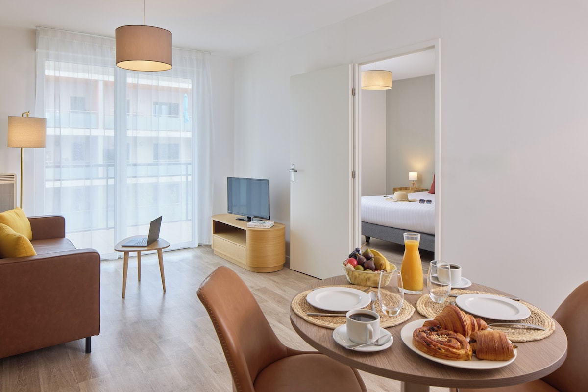 A hotel room with a dining area, a sofa, a TV, and a bed.