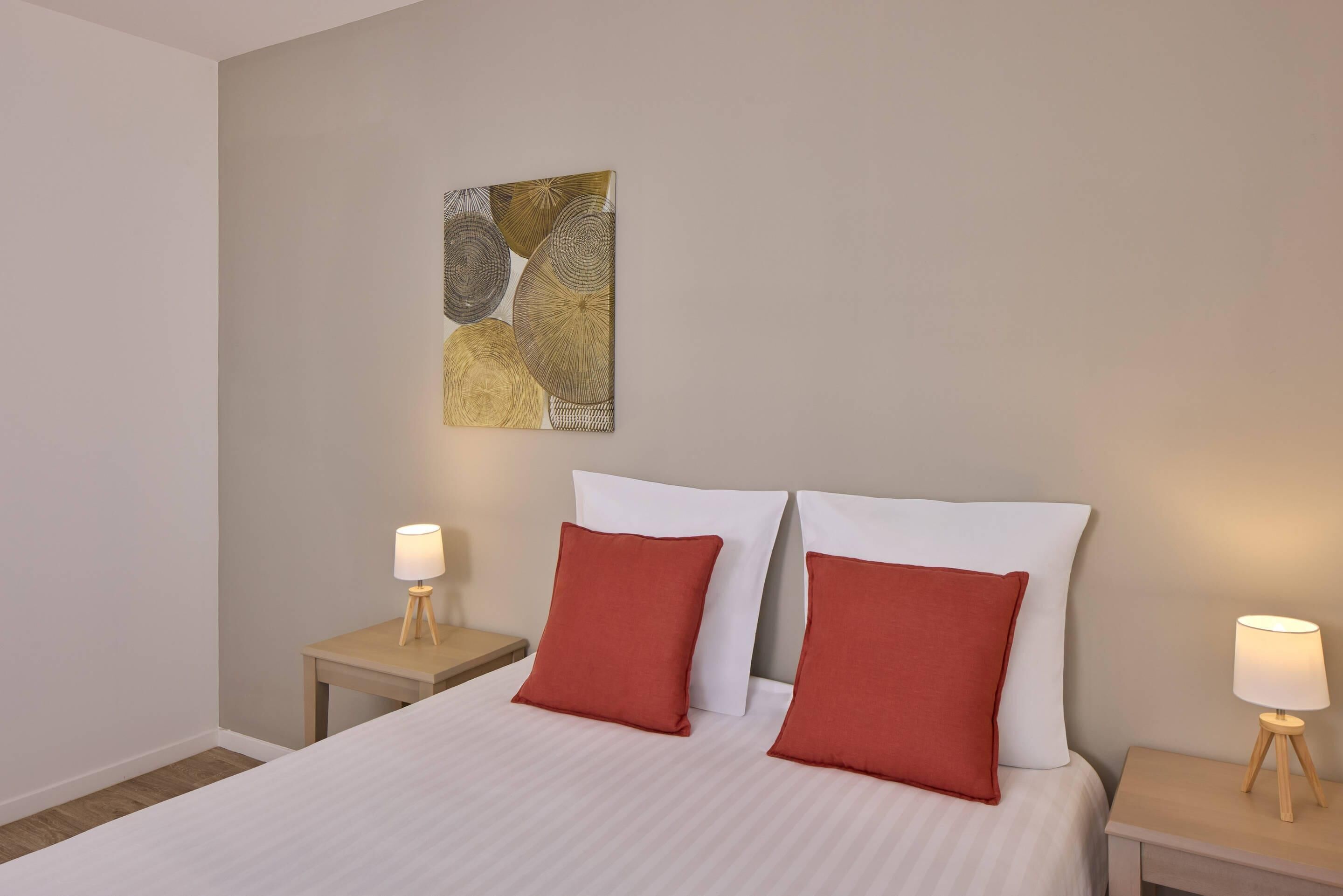 A hotel room with a bed, two nightstands, and a wall art piece.