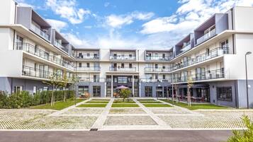 A modern multi-story residential building with balconies, a central courtyard, and a clear sky.