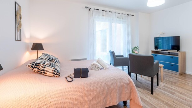 Un dormitorio con cama, escritorio, silla, televisor y ventana con persianas.