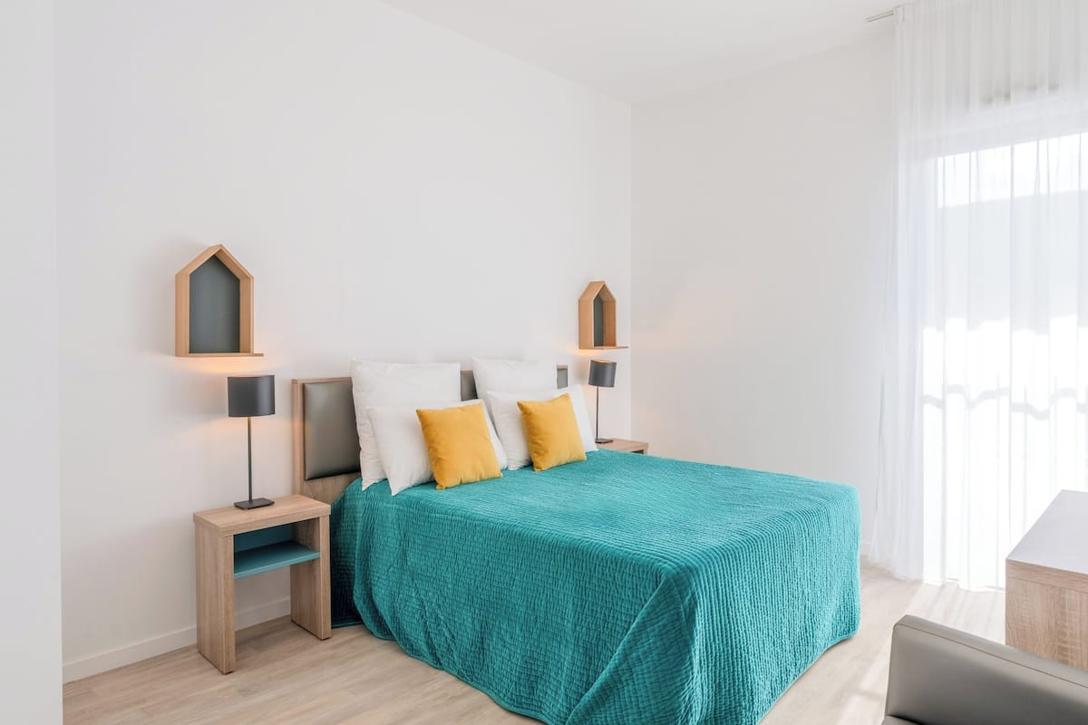 Una camera da letto moderna con una coperta color petrolio, comodini in legno e una scrivania.