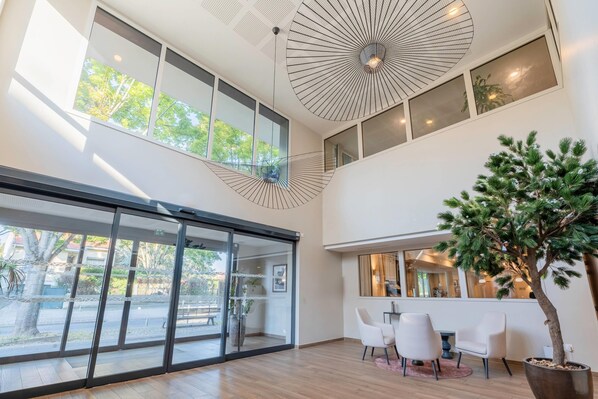 A modern interior with large windows, a ceiling fan, and a potted tree. - Quality Aparthotel Parc Marne la Vallée (Bailly-Romainvilliers)