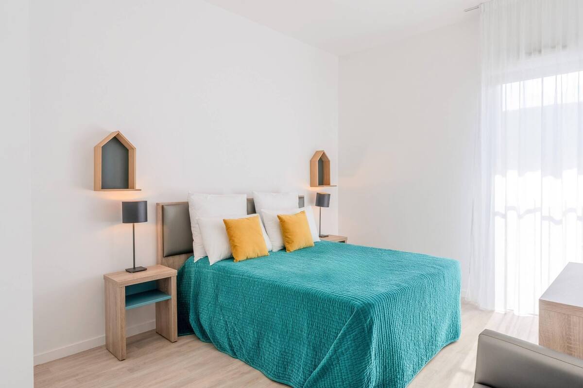 Una camera da letto moderna con una copriletto color petrolio, comodini in legno e una scrivania.