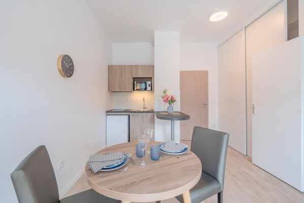 Una cocina compacta con electrodomésticos modernos, una mesa de comedor con sillas y una mesita auxiliar con un jarrón.