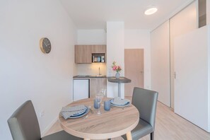 Une cuisine compacte dotée d’appareils électroménagers modernes, une table à manger avec des chaises et une petite table d’appoint sur laquelle est posé un vase.