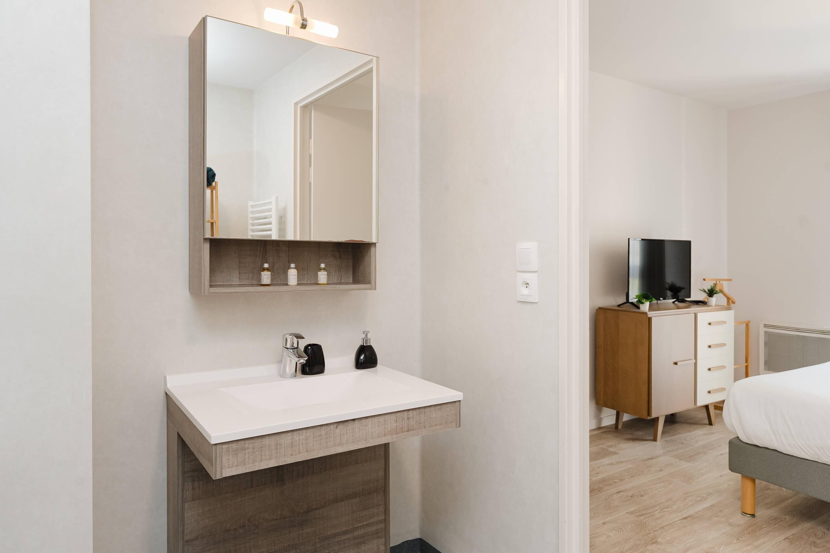A modern bathroom with a white sink, a mirror, and a wooden vanity.