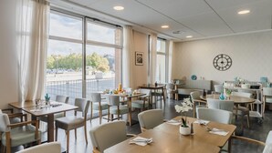 A spacious dining area with multiple tables and chairs, large windows with curtains, a clock on the wall, and a view of the outside. - Quality Aparthotel Dinan (Dinan)