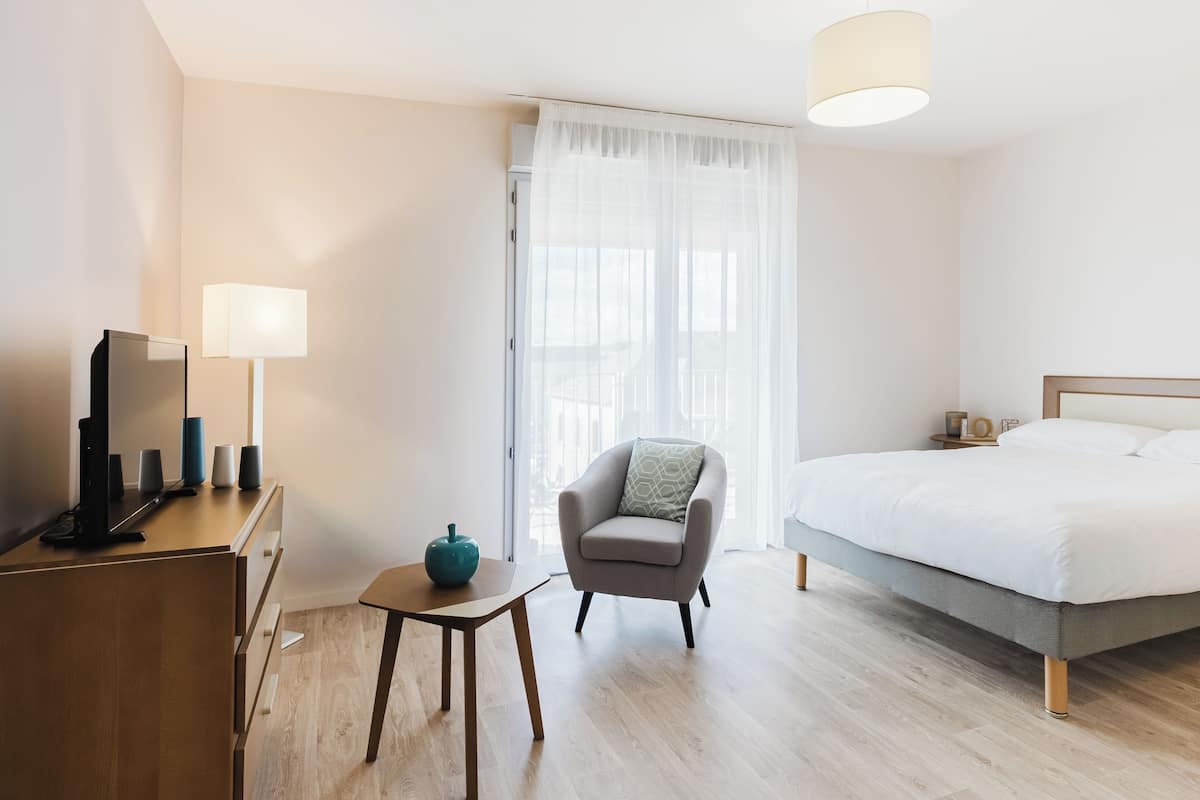 A hotel room with a bed, a desk with a computer, a chair, and a lamp.
