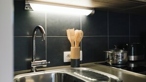A kitchen with a stainless steel sink, a wooden utensil holder, and a pot on the stove. - Quality Aparthotel Dinan (Dinan)