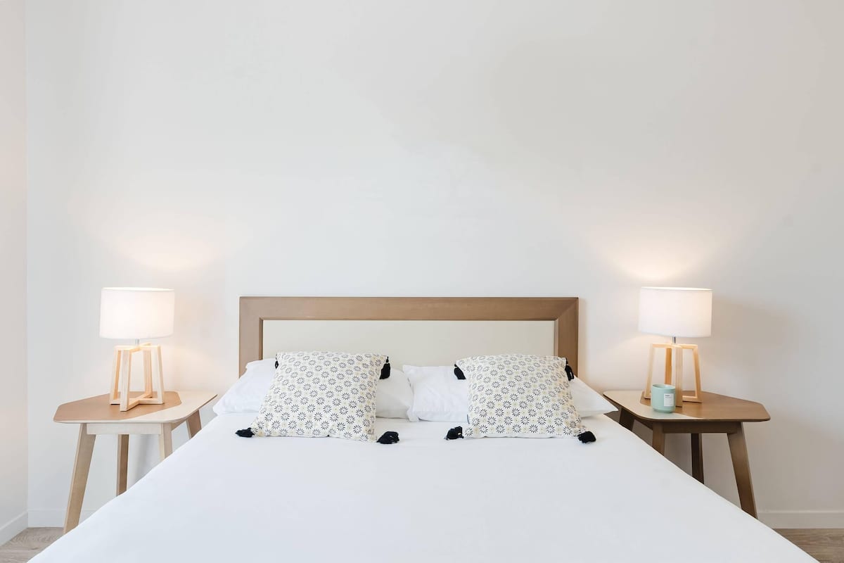 A neatly made bed with a wooden headboard, two bedside tables with lamps, and patterned pillows.