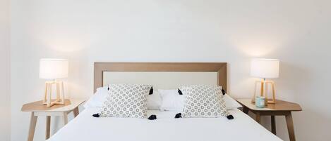 Un lit bien fait, avec une tête de lit en bois, deux tables de chevet avec des lampes et des coussins à motifs.