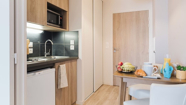 A modern kitchen with wooden cabinets, a built-in microwave, a sink, and a dining area with a table set for breakfast. - Quality Aparthotel Dinan (Dinan)