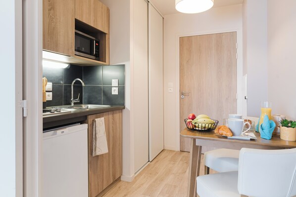 A modern kitchen with wooden cabinets, a built-in microwave, a sink, and a dining area with a table set for breakfast. - Quality Aparthotel Dinan (Dinan)