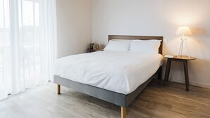 A neatly made bed with white linens, a wooden headboard, and a bedside table with a lamp. - Quality Aparthotel Dinan (Dinan)