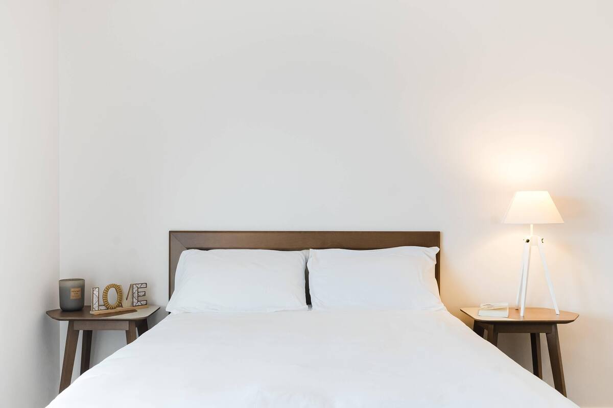 A neatly made bed with white linens, a bedside table with a lamp, and a small decorative item on the nightstand.