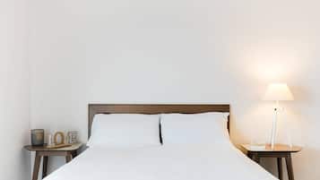 A neatly made bed with white linens, a bedside table with a lamp, and a small decorative item on the nightstand.