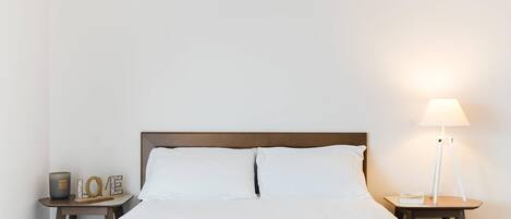 A neatly made bed with white linens, a bedside table with a lamp, and a small decorative item on the nightstand.
