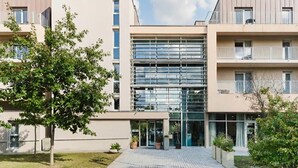 A modern apartment building with a central glass facade, multiple balconies, and a well-maintained garden area. - Quality Aparthotel Dinan (Dinan)