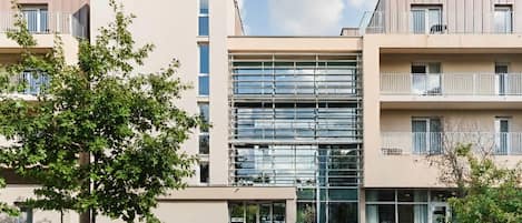 En moderne lejlighedskompolex med en central glasfacade, flere balkoner og en velholdt have.