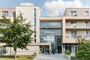 A modern apartment building with a central glass facade, multiple balconies, and a well-maintained garden area. - Quality Aparthotel Dinan (Dinan)