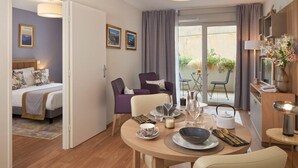 A modern hotel room with a bed, a dining table set for two, a sofa, and a balcony with a table and chairs. - Quality Aparthotel Seyssinet (Seyssinet-Pariset)
