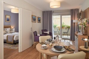 A modern hotel room with a bed, a dining table set for two, a sofa, and a balcony with a table and chairs. - Quality Aparthotel Seyssinet (Seyssinet-Pariset)