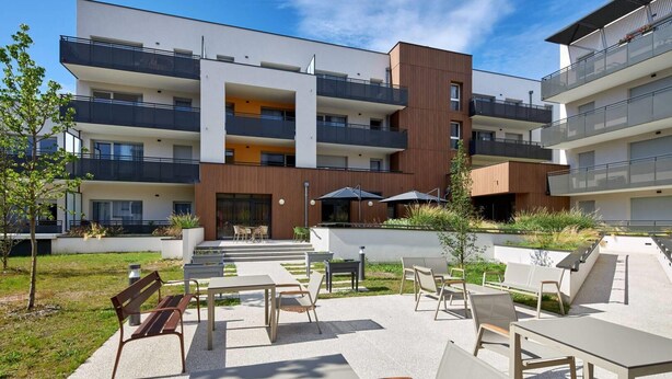 A modern apartment building with outdoor seating and a garden area. - Quality Aparthotel Seyssinet (Seyssinet-Pariset)