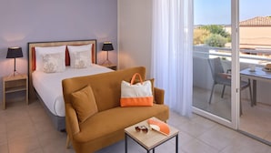 A hotel room with a bed, a sofa, a table with a fan, and a balcony with a table and chairs. - Quality Aparthotel Seyssinet (Seyssinet-Pariset)