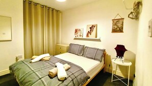 Een netjes opgemaakt bed met kussens, een nachtkastje met een lamp en kunst aan de muur.