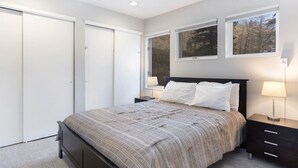 Une chambre à coucher comprenant un lit, deux tables de chevet, une armoire et deux fenêtres.